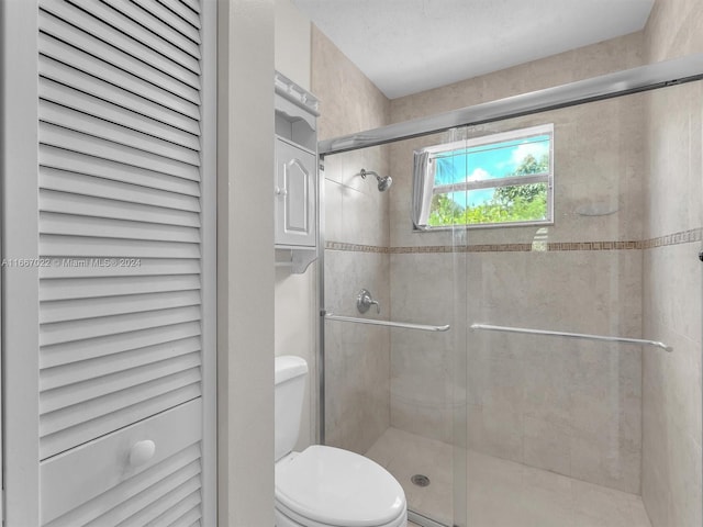 bathroom featuring a shower with door and toilet