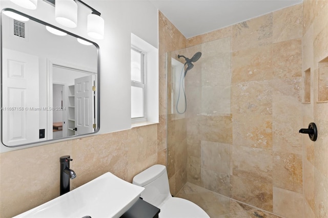 bathroom featuring tiled shower, toilet, tile walls, and sink