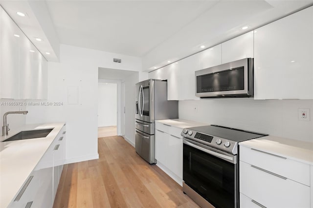 kitchen with light wood-type flooring, sink, decorative backsplash, appliances with stainless steel finishes, and white cabinetry