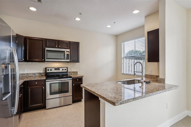 kitchen with dark brown cabinets, sink, kitchen peninsula, appliances with stainless steel finishes, and light stone countertops