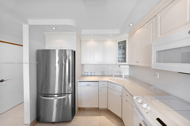 kitchen with white appliances, light tile patterned flooring, sink, and white cabinets