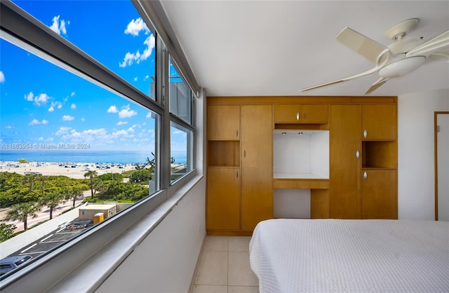 bedroom featuring a view of the beach, a water view, ceiling fan, and light tile patterned floors