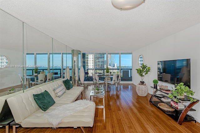 living room with a textured ceiling, a water view, floor to ceiling windows, and hardwood / wood-style flooring