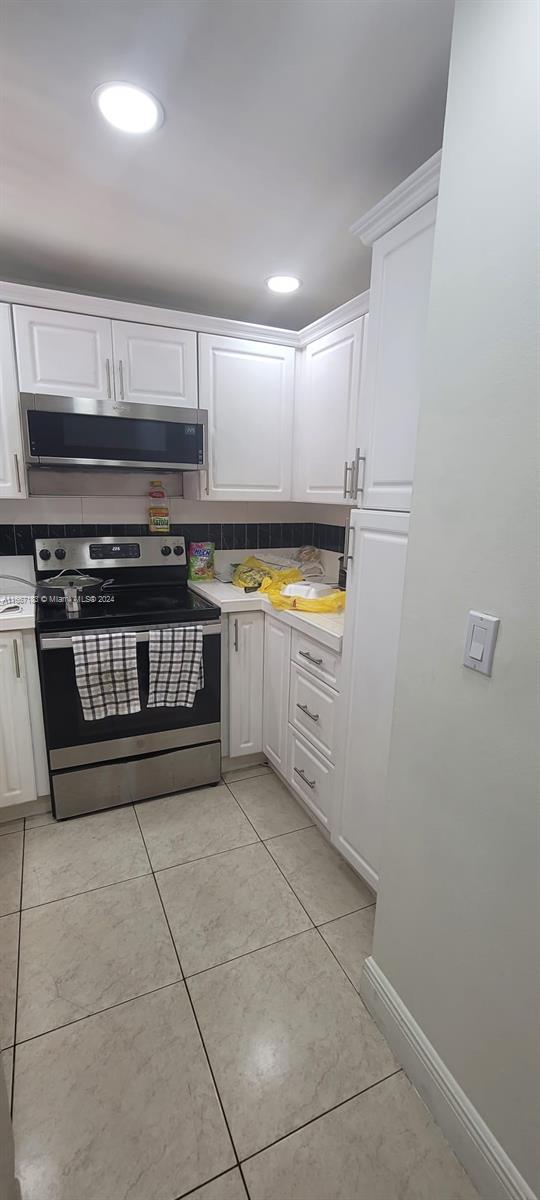 kitchen with ventilation hood, light tile patterned floors, white cabinetry, and stainless steel electric range