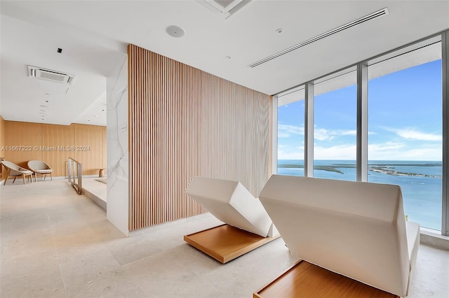 living area with floor to ceiling windows, a water view, and wood walls