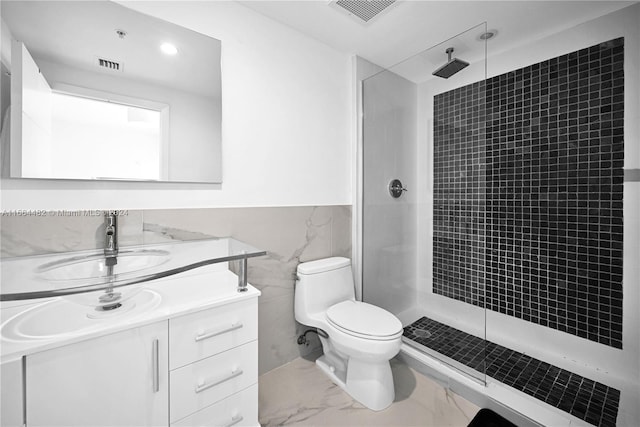 bathroom featuring tile walls, tiled shower, vanity, and toilet