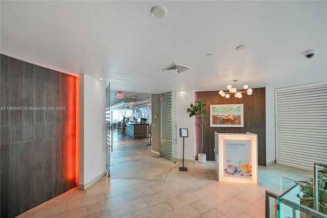 hall featuring an inviting chandelier and wood walls