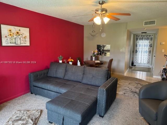 living room with ceiling fan, a textured ceiling, and light carpet