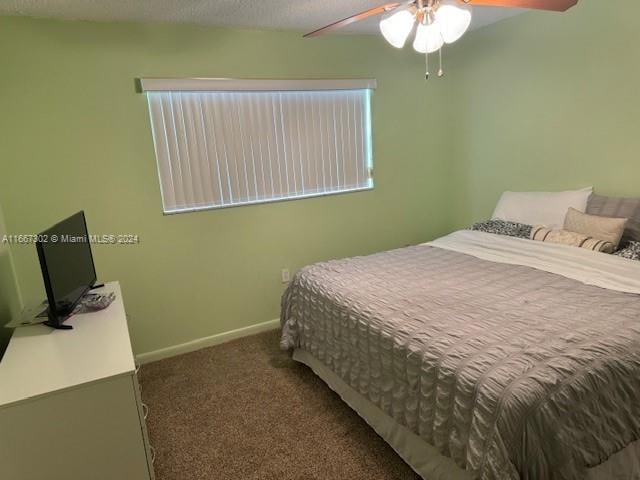 bedroom featuring a textured ceiling, dark colored carpet, and ceiling fan