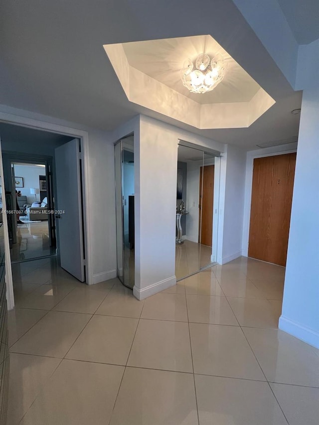 corridor featuring a tray ceiling and light tile patterned floors