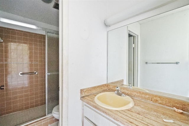 bathroom featuring a textured ceiling, vanity, toilet, and a shower with shower door