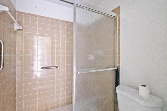 bathroom featuring a shower with door and toilet