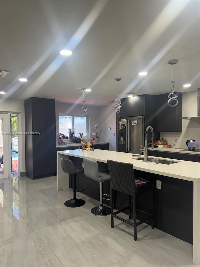 kitchen with hanging light fixtures, stainless steel refrigerator with ice dispenser, sink, and a kitchen island with sink