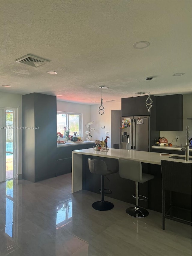 kitchen featuring a breakfast bar, stainless steel fridge, sink, pendant lighting, and a textured ceiling