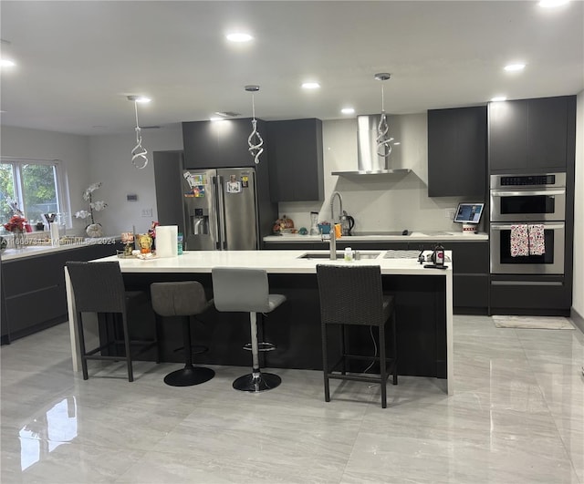 kitchen featuring a center island with sink, decorative light fixtures, stainless steel appliances, and a breakfast bar