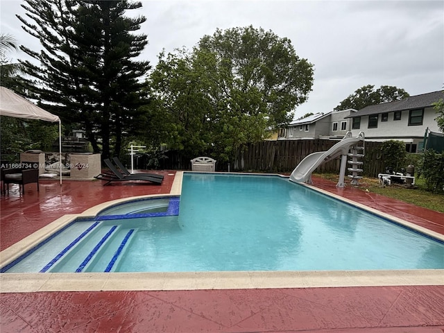 view of pool with an in ground hot tub, a water slide, and a patio area