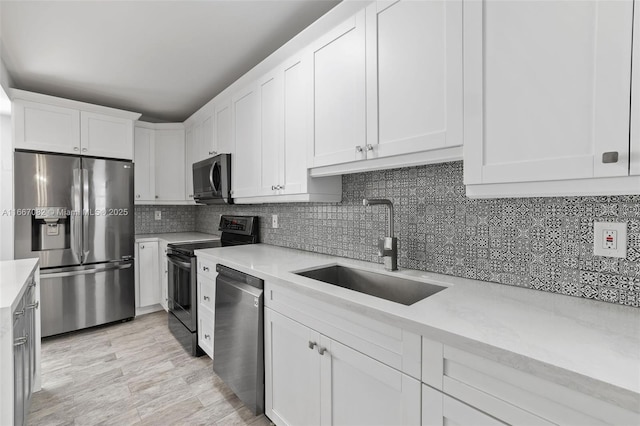 kitchen with sink, appliances with stainless steel finishes, light hardwood / wood-style floors, white cabinets, and decorative backsplash