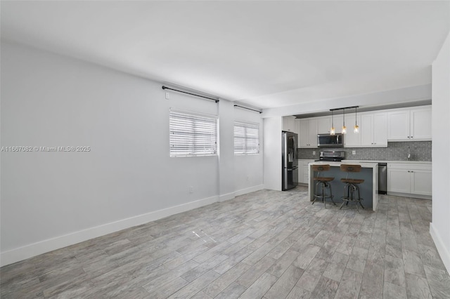 kitchen with white cabinetry, stainless steel appliances, pendant lighting, light hardwood / wood-style floors, and a breakfast bar