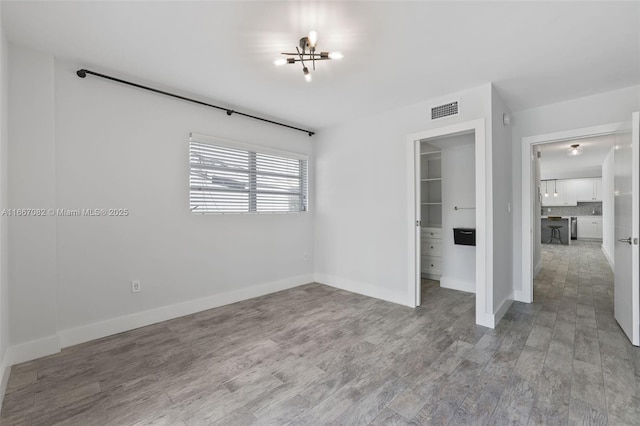 unfurnished bedroom with a chandelier, hardwood / wood-style flooring, a spacious closet, and a closet