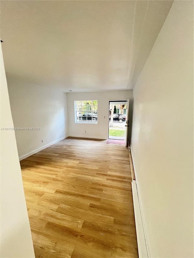 unfurnished room featuring light wood-type flooring, baseboards, and a baseboard radiator