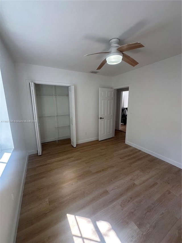 unfurnished bedroom with wood finished floors, visible vents, a closet, and baseboards