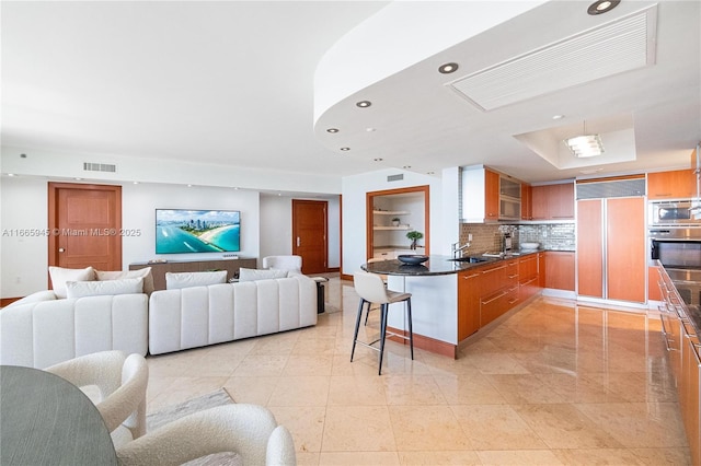 kitchen featuring sink, built in appliances, a kitchen breakfast bar, kitchen peninsula, and backsplash