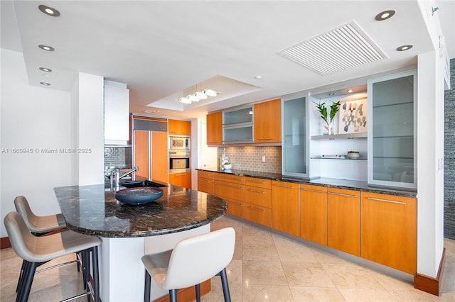 kitchen with a kitchen bar, sink, built in appliances, light tile patterned floors, and backsplash