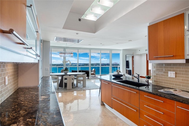 kitchen featuring sink, dark stone countertops, backsplash, hanging light fixtures, and a water view