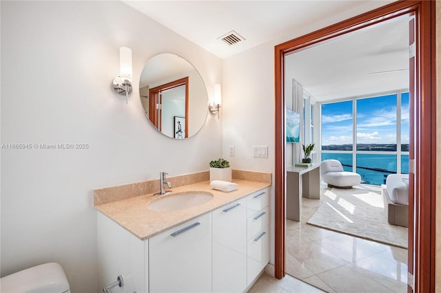 bathroom with a wall of windows, vanity, toilet, a water view, and tile patterned floors