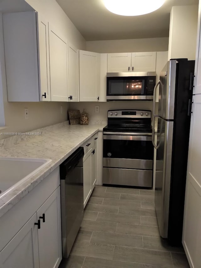 kitchen featuring white cabinets, light wood-type flooring, stainless steel appliances, and light stone counters