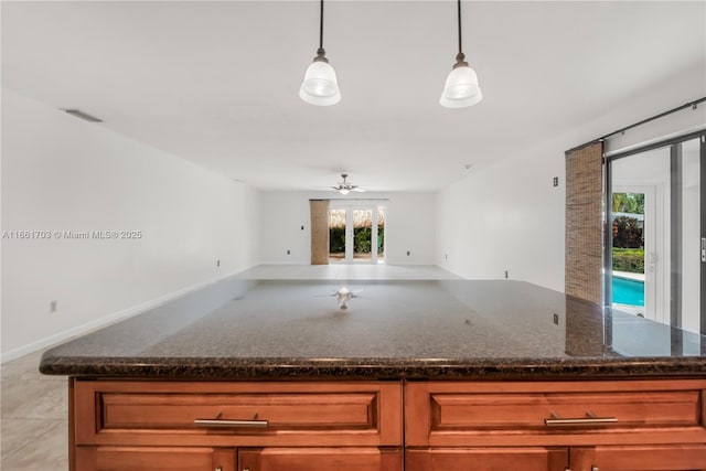 kitchen with visible vents, brown cabinetry, open floor plan, dark stone countertops, and pendant lighting