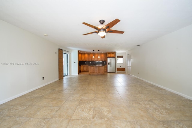 unfurnished living room featuring ceiling fan and baseboards