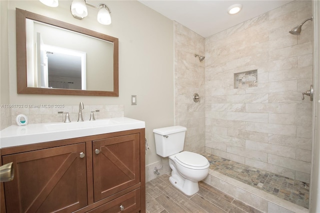 full bathroom featuring toilet, a tile shower, backsplash, and vanity