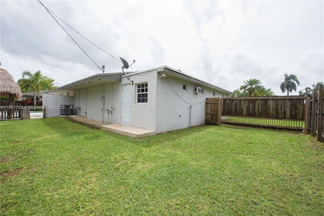 rear view of house featuring a wall unit AC, central air condition unit, fence, a yard, and stucco siding