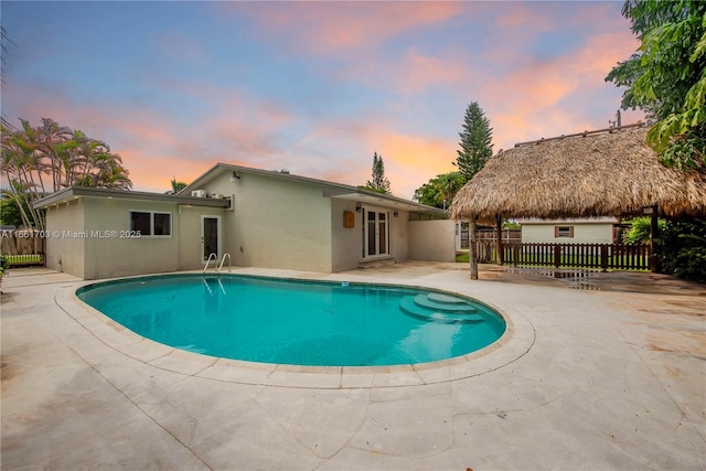 pool at dusk with a patio area, fence, and a fenced in pool