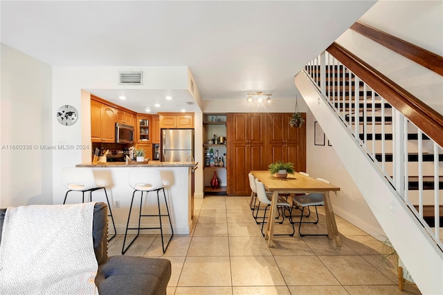 kitchen with appliances with stainless steel finishes, kitchen peninsula, light tile patterned floors, and a kitchen bar