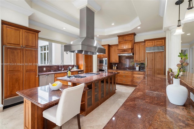 kitchen with hanging light fixtures, island range hood, built in appliances, decorative columns, and decorative backsplash