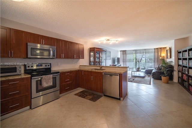 kitchen featuring a textured ceiling, sink, kitchen peninsula, decorative backsplash, and stainless steel appliances