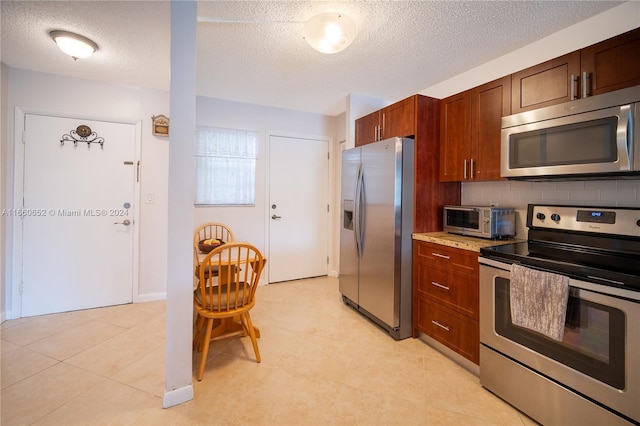 kitchen with appliances with stainless steel finishes, decorative backsplash, light tile patterned flooring, light stone countertops, and a textured ceiling