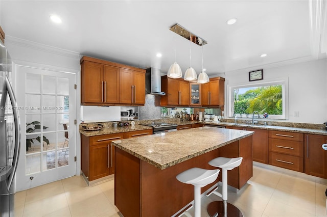 kitchen with hanging light fixtures, sink, a breakfast bar, wall chimney exhaust hood, and stainless steel range oven