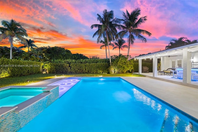 pool at dusk with an in ground hot tub and a patio area