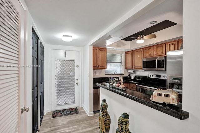 kitchen with appliances with stainless steel finishes, dark stone countertops, backsplash, ceiling fan, and light hardwood / wood-style flooring