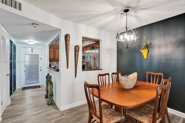 dining room with light hardwood / wood-style flooring, a textured ceiling, and an inviting chandelier