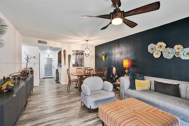 living room featuring hardwood / wood-style flooring, ceiling fan with notable chandelier, and a textured ceiling