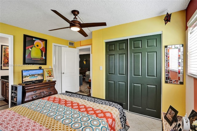 bedroom featuring a textured ceiling, light tile patterned floors, ceiling fan, and a closet