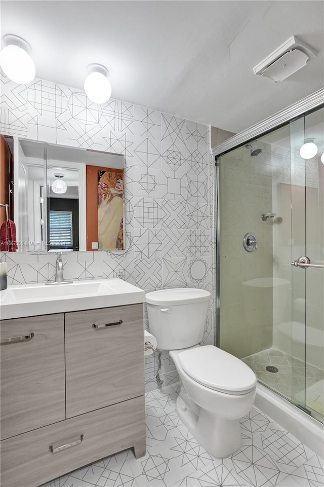 bathroom featuring tile walls, vanity, toilet, and a shower with shower door