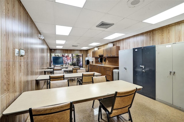 dining room featuring a paneled ceiling, wooden walls, and sink