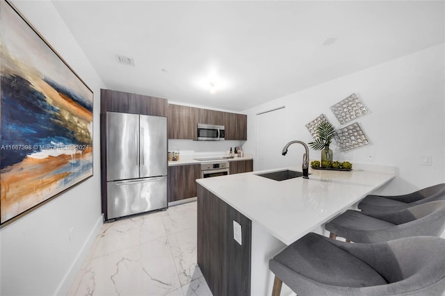 kitchen with dark brown cabinets, sink, kitchen peninsula, a kitchen bar, and appliances with stainless steel finishes