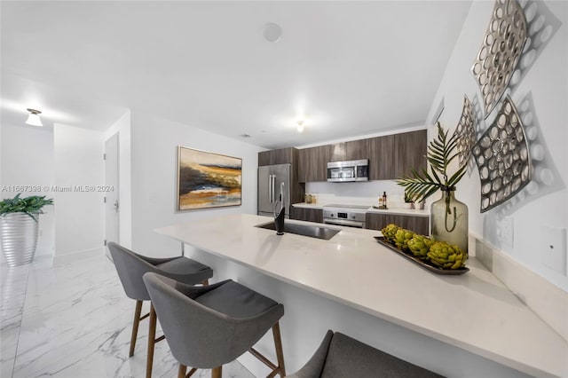 kitchen featuring appliances with stainless steel finishes, a kitchen breakfast bar, kitchen peninsula, dark brown cabinetry, and sink