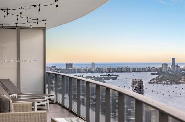 balcony at dusk featuring a water view